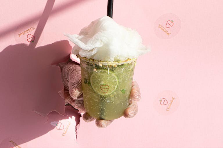 A hand holding a lime drink with cotton candy against a pink wall, symbolizing freshness.