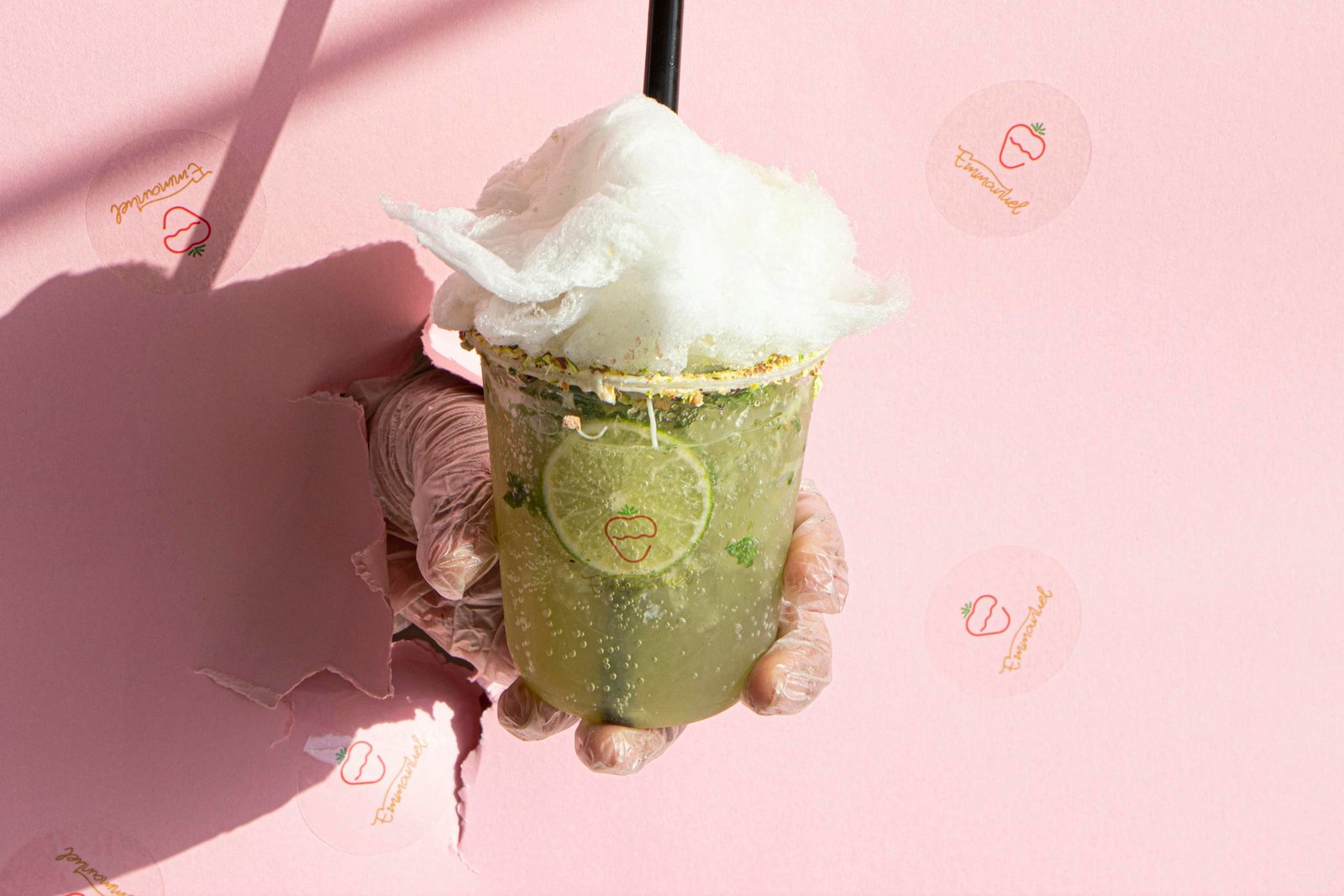 A hand holding a lime drink with cotton candy against a pink wall, symbolizing freshness.