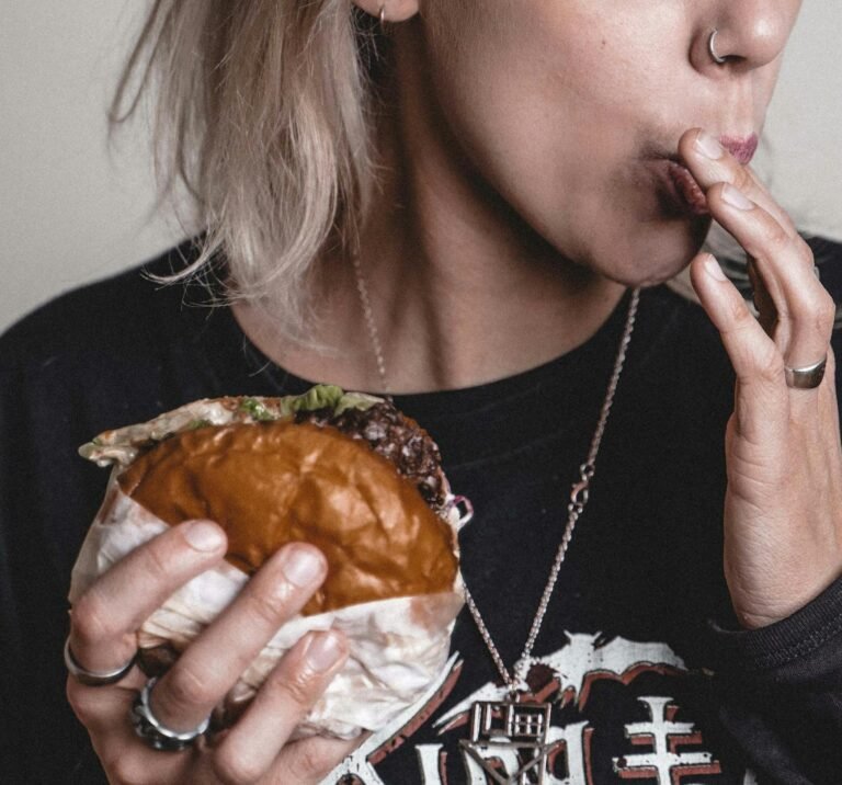 A woman savoring a delicious beef burger, featuring a close-up of her tattooed hand and rings.