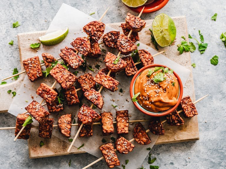 Appetizing grilled tempeh skewers paired with a rich, spicy peanut sauce, garnished with fresh herbs.