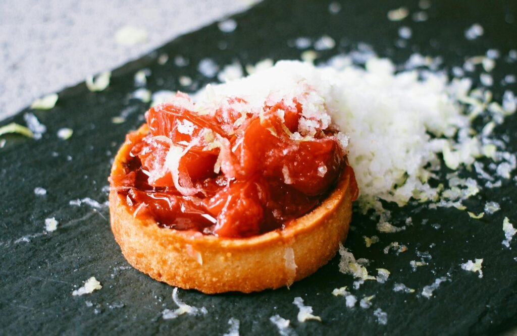 A close-up of a tart topped with tomatoes and cheese on a slate plate.