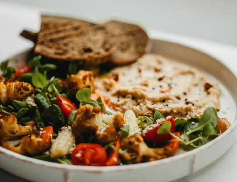 A vibrant vegan salad with roasted vegetables and bread in a cozy setting.