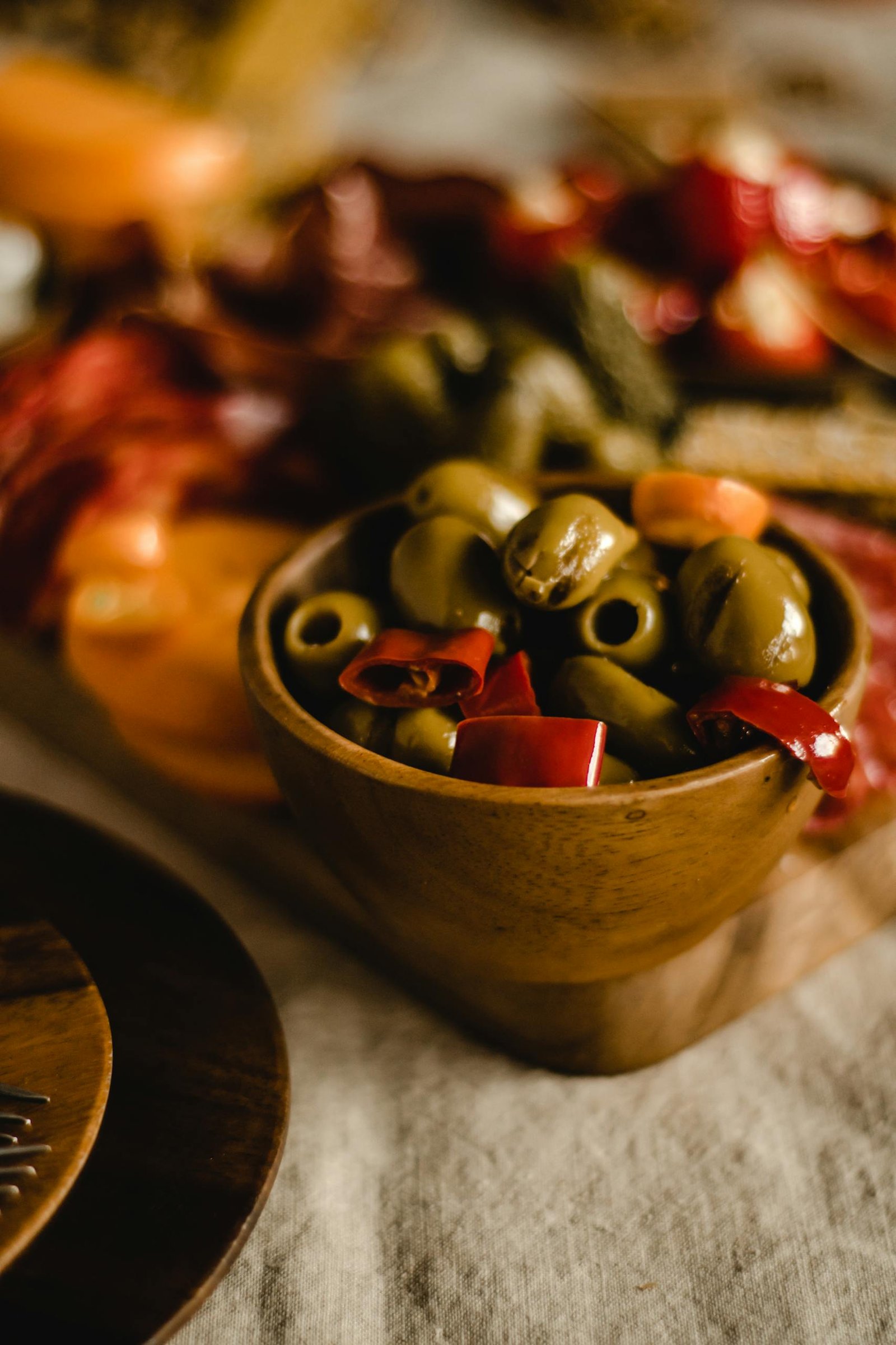 Close-up of a rustic wooden bowl filled with fresh olives and peppers in a cozy setting.