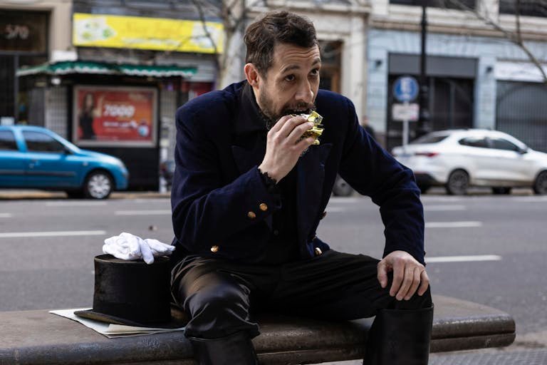 Gentleman in classic clothing enjoys a snack on a busy Buenos Aires street.