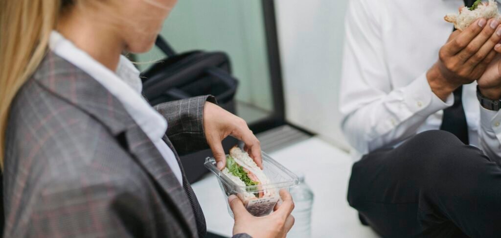 Two professionals in business attire enjoy sandwiches during a lunch break. Perfect for office and lifestyle themes.